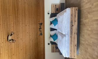 A modern bedroom with a large wooden bed and cozy pillows. The wooden ceiling gives the room a warm atmosphere.
