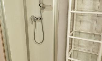 A modern shower in a bathroom. Next to the shower is a white shelving system.