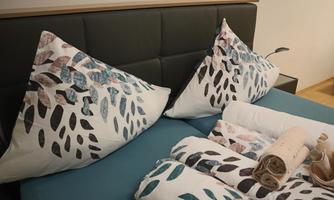 A modern bedroom with a bed and decorative cushions in leaf design. White towels are neatly placed on the bedspread.
