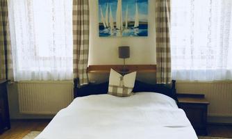 A cozy bedroom with a large bed and bright light. On the wall hangs a picture of sailboats, and the windows are decorated with curtains.