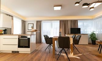 A modern apartment with an open kitchen and dining area. Large windows provide plenty of light and a cozy atmosphere.