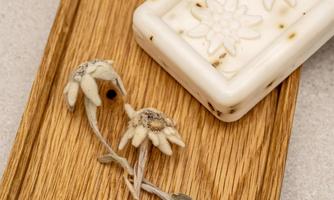 An elegant wooden board with a soap in the shape of a flower and dried flowers. The arrangement conveys a natural and minimalist aesthetic.