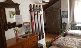 A cozy room with two beds, a wardrobe, and a wooden chest of drawers. Skis and a beautiful wall decoration hang on the wall.