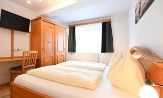 A cozy bedroom with a double bed and a large window. The room is furnished with wooden furniture and equipped with a television.