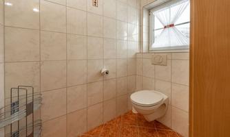 A small, brightly tiled bathroom with a white toilet. A window brings daylight into the room.