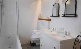 A modern bathroom with a bathtub, two sinks, and elegant mirrors. The walls are brightly tiled and the floor is gray.