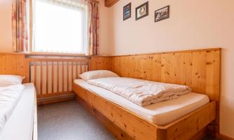 A simple bedroom with two wooden beds and a large window. The walls are light, and there are some pictures that are decoratively placed.