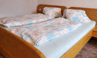 A wooden bed with a blue bed sheet and floral blankets. Two pillows are also present, enhancing the cozy atmosphere.