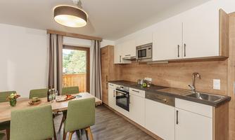 A modern kitchen with wood decor and light furniture. The dining area is cozy, with a table and green chairs.