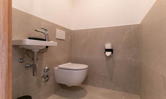 A modern bathroom with a stylish sink and a wall-mounted toilet. The walls are lined with smooth, light tiles.