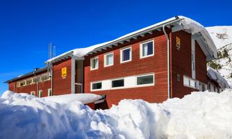 A red building in a wintry landscape, surrounded by lots of snow. The clear blue sky creates a vibrant atmosphere.