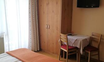 A cozy room with two beds and an orange throw. There is a table with chairs and a television on the wall.