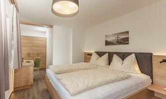 A bright room with two single beds and modern wooden decor. The furnishings are simple and cozy, ideal for a relaxing stay.