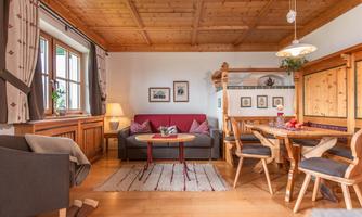 A cozy living space with a wooden ceiling and a sofa. There are chairs at the table, and there is decoration on the walls.