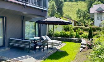 A cozy terrace with a seating area and a sun umbrella. The green garden and the surrounding hills create a relaxed atmosphere.