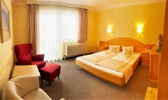 A bright hotel room with two beds and a comfortable armchair. The large window front provides plenty of daylight.