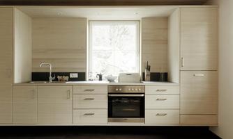 A modern kitchen with wooden cabinets and a cooktop. The large window brings a lot of light into the room.