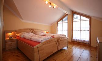 A cozy bedroom with a double bed and two windows. The wooden floor and warm walls create an inviting atmosphere.