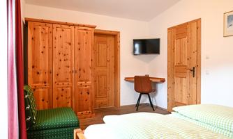 A cozy room with wooden furniture and a double bed. A TV hangs on the wall and a desk is also available.