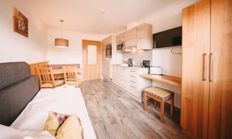 A modern room with a small kitchenette. There is a dining table, a chair, and a cozy seating area.