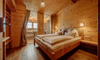 A cozy bedroom with wooden walls and a double bed. The windows let in plenty of light and create an inviting atmosphere.