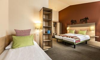 A modern room with two beds and colorful cushions. The room has a warm color tone and features an open wardrobe.