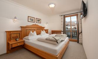 A cozy bedroom with a double bed and wooden paneling. The room has a window overlooking a balcony and beautiful wall paintings.