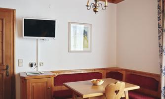 A cozy seating area with a table and upholstered benches. A television and a piece of artwork hang on the wall.
