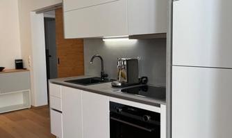 A modern kitchen with white cabinets and a black stove. It is brightly and minimally designed.