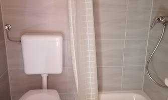A small bathroom with a shower and a toilet. The walls are brightly tiled and the floor is made of wood.