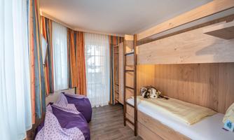 A cozy bedroom with a bunk bed and two bean bags. Large windows let in plenty of daylight.