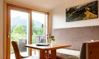 A cozy room with a table, chairs, and a large window. The view of the greenery and the modern decor create an inviting atmosphere.