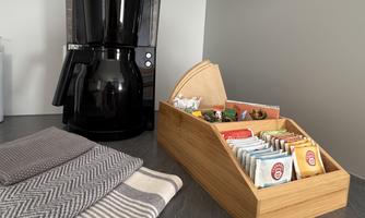 A coffee machine stands next to a wooden box with various types of tea. Several towels lie on the table.