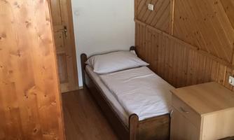 A simple room with two single beds and a wooden piece of furniture. There is a table and a wooden wardrobe.