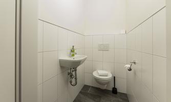 A modern bathroom with white tiles and a sink. It includes a toilet and an elegant fixture.