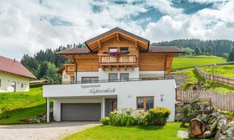 A charming apartment building with a wood and plaster facade, surrounded by green meadows. The tranquil rural setting offers a view of the mountains.