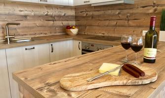 A modern kitchen with wooden shelves and a large wooden countertop. On the table are cheese, sausage, and two glasses of red wine.