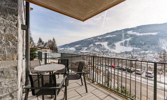 A balcony with a table and chairs offers a view of the snow-capped mountains. The surroundings are quiet and close to nature.