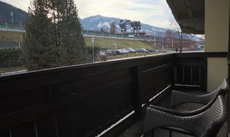 A balcony with two comfortable chairs and a view of a green landscape. In the background, mountains and a clear sky can be seen.