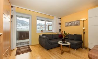 A cozy living room with a gray sofa and a coffee table. The windows offer a view of the mountains, and the walls are painted in soft colors.