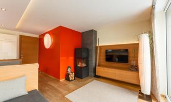 A modern living room with a red wall and a cozy seating area. In the background, there is a television and a fireplace, creating an inviting atmosphere.