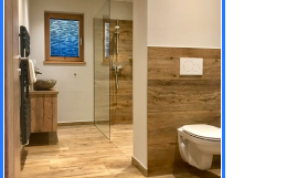 A modern bathroom with wood paneling and elegant tiles. The shower is open and a window brings in natural light.