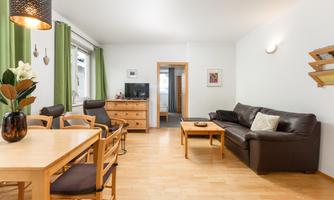 A bright and inviting living space with a cozy couch and a dining area. Large windows with green curtains provide plenty of daylight.