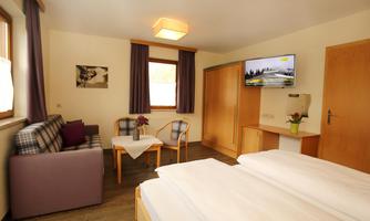 A cozy room with two single beds, a small table and armchair. A television and a window provide pleasant light.
