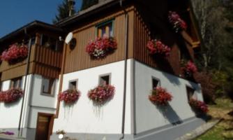 A charming house with wooden cladding and colorful flower boxes. The garden is well-maintained and creates an inviting atmosphere.