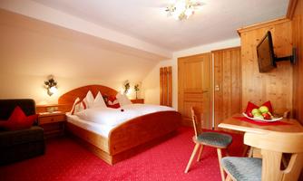 A cozy hotel room with wooden furniture and a red carpet. There is a double bed, a table, and a television.