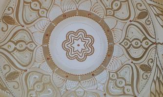 An artistic pattern in golden and white hues. It features a symmetrical design with floral motifs and a central star.