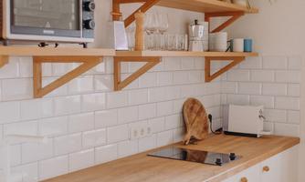 A modern kitchen with white cabinets and wooden shelves. Kitchen appliances, glasses, and plants are on the countertop.