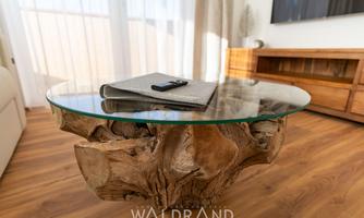 A unique coffee table made of wood with a transparent glass top. On the table are a notebook and a remote control.