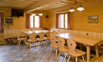 A cozy room with wood paneling and beige tables. Illuminated by large windows and warm lamps, it offers space for sitting and dining.